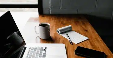 MacBook Pro, white ceramic mug,and black smartphone on table