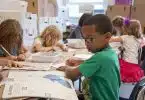 boy in green sweater writing on white paper