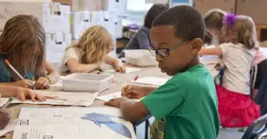 boy in green sweater writing on white paper